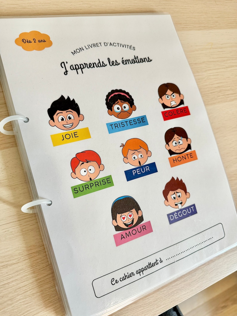 May include: A white booklet with a colorful illustration of faces expressing different emotions. The title of the booklet is "J'apprends les &eacute;motions" which translates to "I learn emotions".