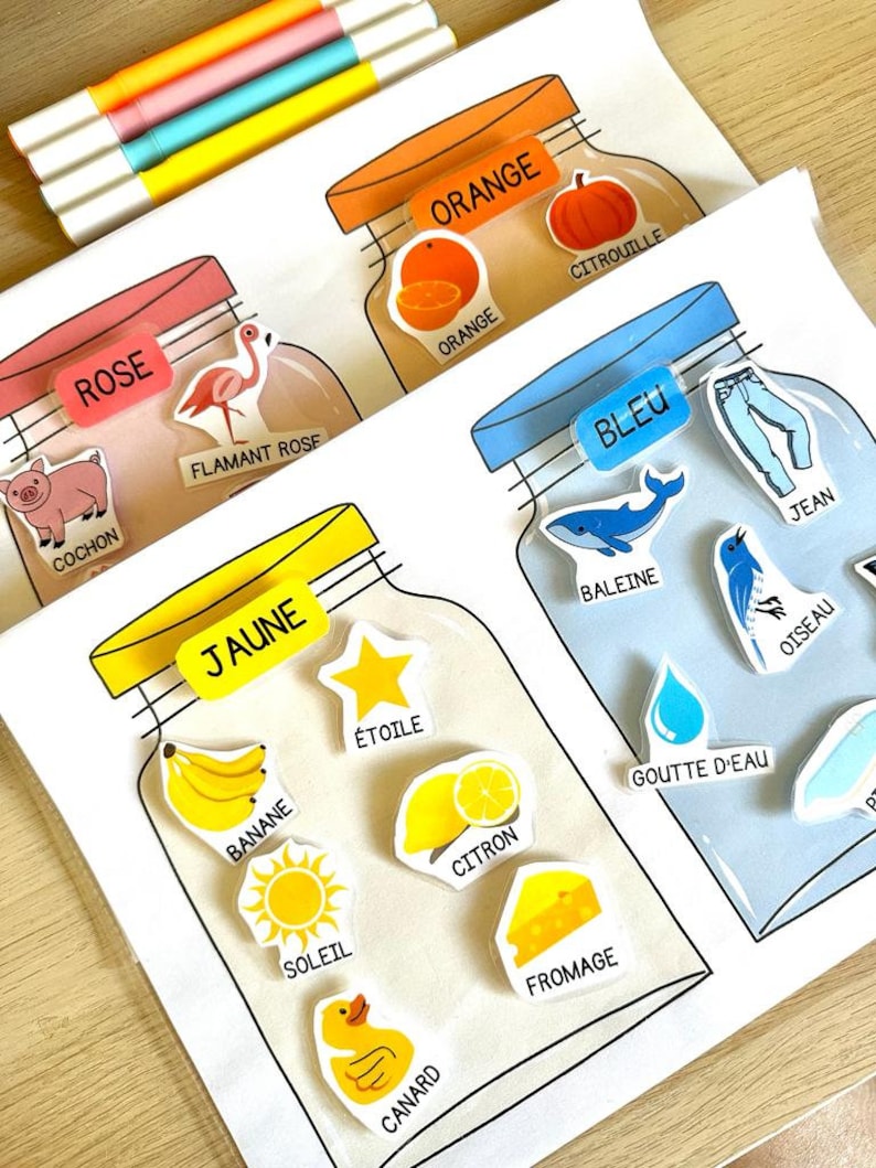 May include: A set of four colourful jars with labels in French. Each jar has a different colour and contains various objects related to that colour. For example, the orange jar contains an orange, a pumpkin, and the word "citrouille" (pumpkin).