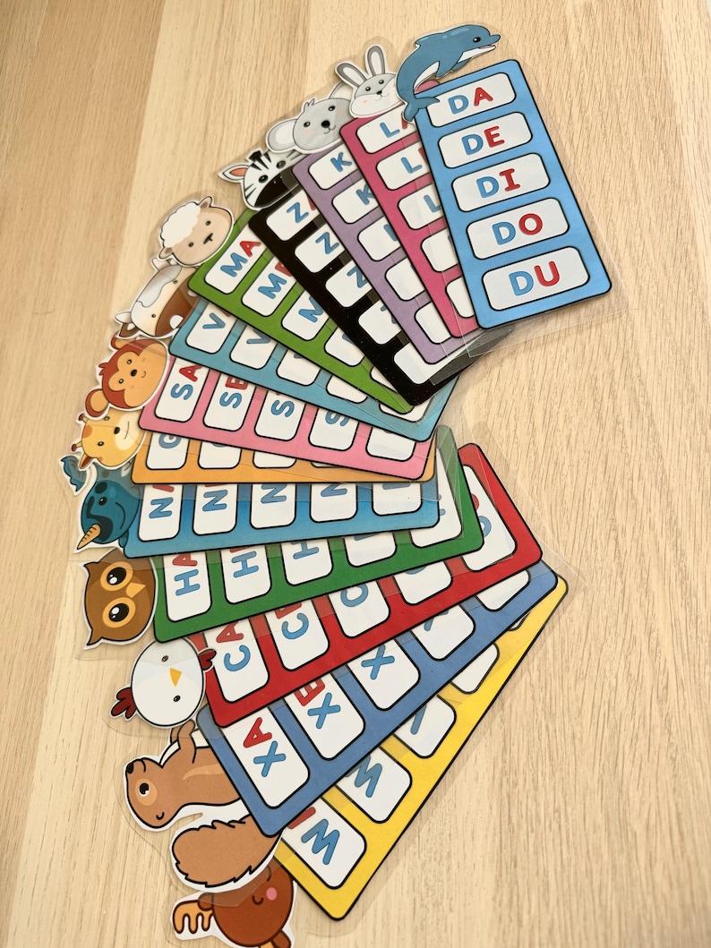 Puede incluir: Un conjunto de tarjetas de memoria coloridas con ilustraciones de animales y letras del alfabeto. Cada tarjeta presenta un animal diferente y una letra, la letra se repite varias veces en la tarjeta. Las tarjetas est&aacute;n dispuestas en forma de abanico, con la tarjeta superior mostrando un delf&iacute;n y las letras DA, DE, DI, DO y DU.