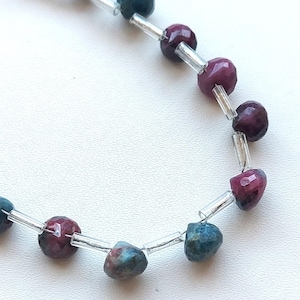 May include: A strand of faceted gemstone beads in shades of green, blue, and pink. The beads are strung on clear thread with silver spacers.