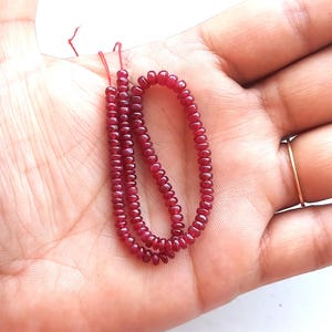 Peut inclure: Un brin de perles de rubis rouge foncé, enfilées sur un fil rouge fin. Les perles sont rondes et lisses, et elles sont disposées en un motif lâche et fluide.