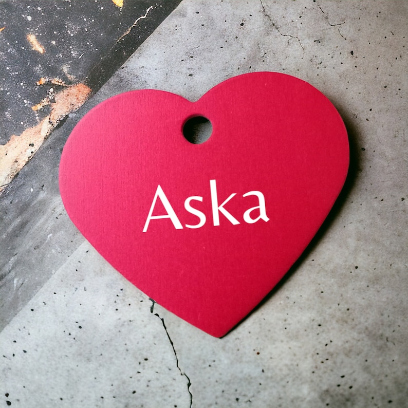 May include: A red heart-shaped tag with the name "Aska" written in white lettering.