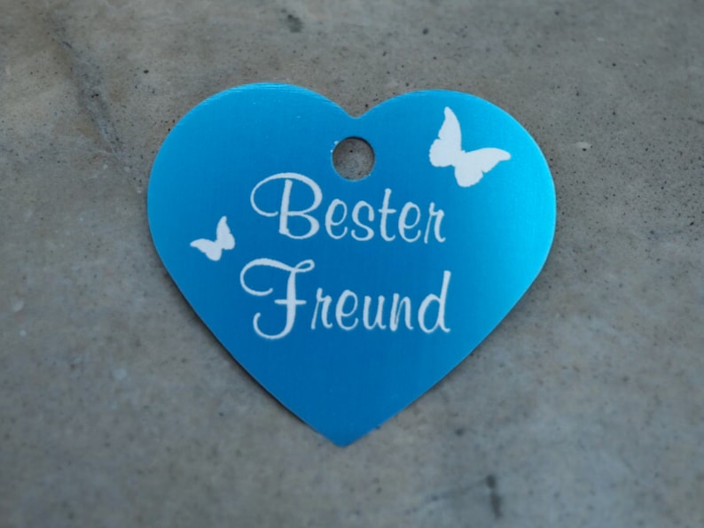 May include: A blue heart-shaped metal tag with the text "Best Friend" and two white butterfly silhouettes.
