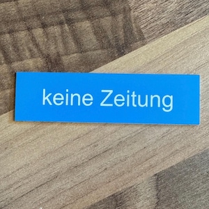 K&ouml;nnte beinhalten: Ein blaues rechteckiges Schild mit wei&szlig;em Text, auf dem "keine Zeitung" steht.