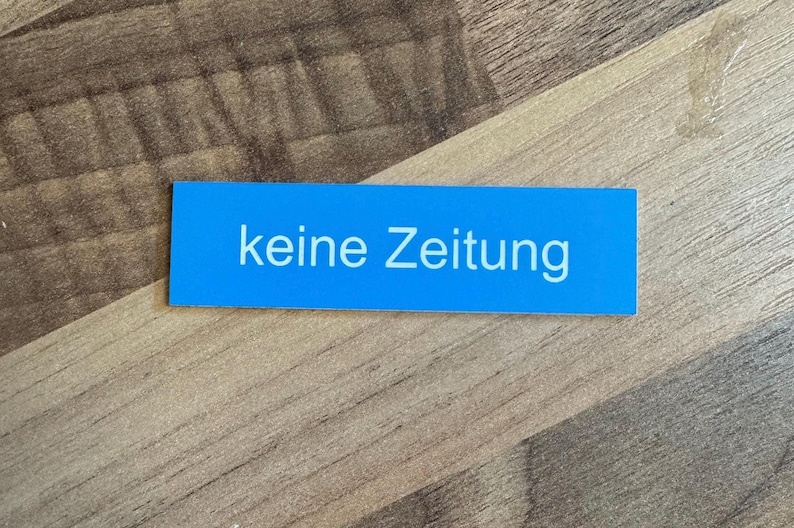 K&ouml;nnte beinhalten: Ein blaues rechteckiges Schild mit wei&szlig;em Text, auf dem "keine Zeitung" steht.