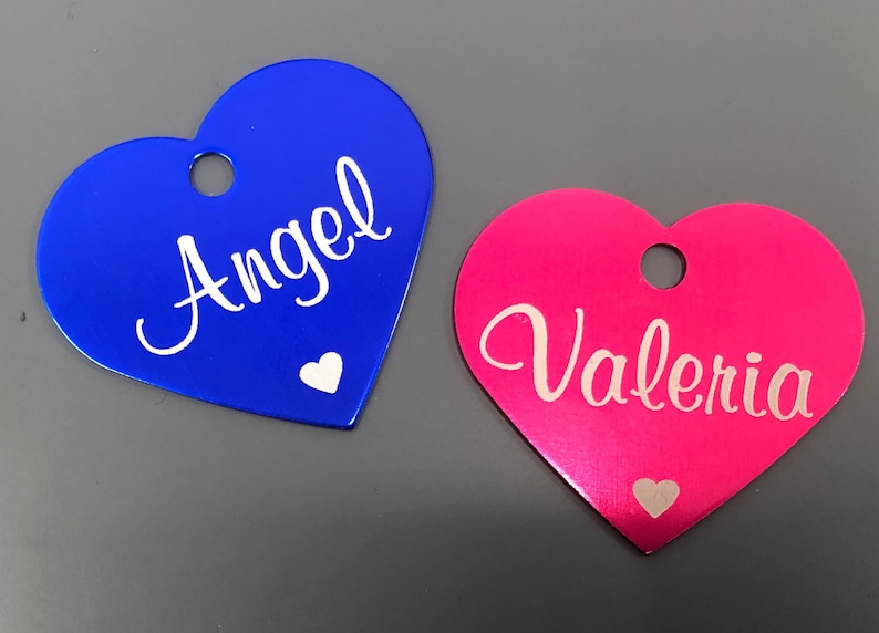 May include: Two heart-shaped metal tags with white lettering. The blue tag says "Angel" and the pink tag says "Valeria".