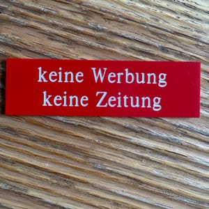 K&ouml;nnte beinhalten: Ein rotes rechteckiges Schild mit wei&szlig;em Text, auf dem "keine Werbung keine Zeitung" steht.