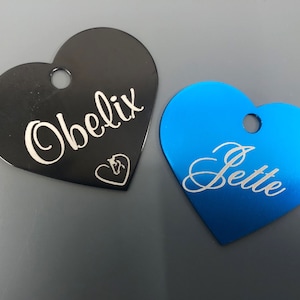 May include: Two heart-shaped pet ID tags, one black with the name "Obelix" and a horse head symbol, and one blue with the name "Jette".