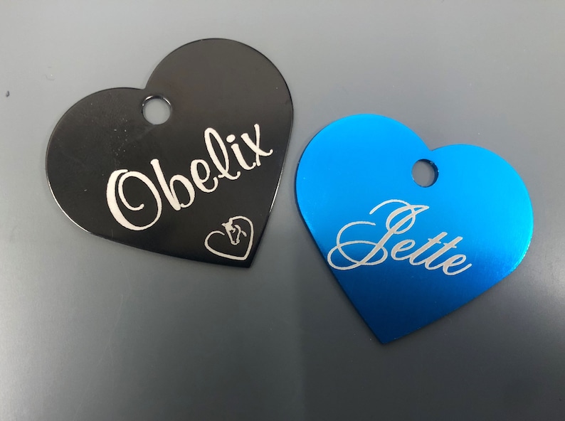 May include: Two heart-shaped pet ID tags, one black with the name "Obelix" and a horse head symbol, and one blue with the name "Jette".