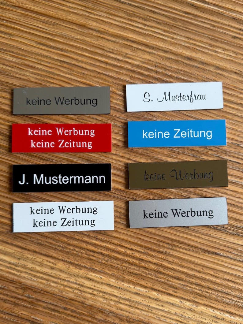 K&ouml;nnte beinhalten: Acht rechteckige Schilder mit schwarzem Text auf verschiedenen farbigen Hintergr&uuml;nden. Die Schilder sagen "keine Werbung" (keine Werbung) und "keine Zeitung" (keine Zeitung). Zwei Schilder haben Namen: "S. Musterfrau" und "J. Mustermann".
