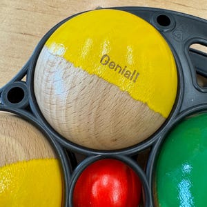 Könnte beinhalten: Ein Satz Holzbälle mit verschiedenen Farben. Ein Ball hat die Aufschrift "Genial!"
