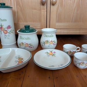 Op de afbeelding: Een set keukendozen en schalen met een groen-wit bloemenpatroon met een fruitmotief. De dozen zijn gelabeld met "Pasta", "Koekjes" en "Keukengerei".