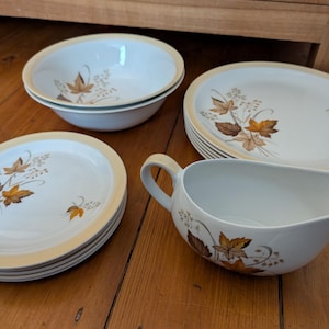 Könnte beinhalten: Ein Set aus weißem Keramikgeschirr mit einem braunen und gelben Blattmotiv. Das Set enthält eine Schüssel, eine Sauciere und drei Teller.