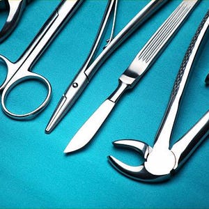 May include: Close-up of various stainless steel surgical instruments, including scissors, scalpels, and forceps, arranged on a teal surface. The tools are highly reflective, suggesting a sterile environment.