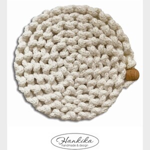 Puede incluir: Gorro de punto crema hecho a mano con un dise&ntilde;o anudado texturizado. El gorro presenta un peque&ntilde;o acento redondo de madera en el lateral. La imagen incluye el texto "Hankika handmade & design" en una fuente decorativa.