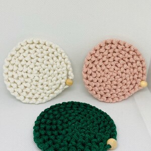 Puede incluir: Tres posavasos de ganchillo hechos a mano en crema, rosa y verde. Cada posavasos es redondo con un detalle de cuentas de madera. Los posavasos est&aacute;n hechos de un hilo grueso y texturizado.