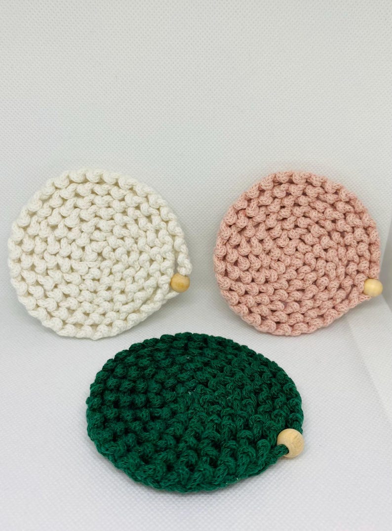 Puede incluir: Tres posavasos de ganchillo hechos a mano en crema, rosa y verde. Cada posavasos es redondo con un detalle de cuentas de madera. Los posavasos est&aacute;n hechos de un hilo grueso y texturizado.