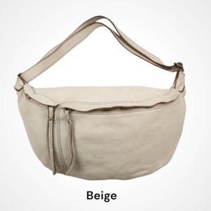 Op de afbeelding: Een beige, halvemaanvormige schoudertas met een gladde textuur, een ritssluiting aan de bovenkant en een verstelbare schouderriem. De tas heeft twee lange leren ritstrekkers aan de voorzijde en metalen accenten in antiek messingkleur.