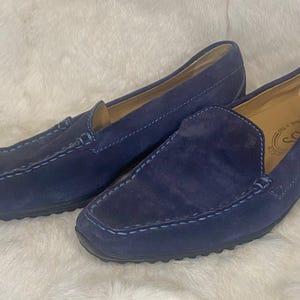 Puede incluir: Un par de mocasines de ante azul marino. Los zapatos tienen una puntera redondeada, un dise&ntilde;o sin cordones y costuras visibles. Las suelas son negras y el interior es de color beige claro.