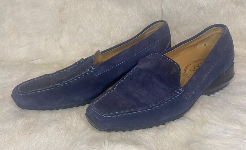Puede incluir: Un par de mocasines de ante azul marino. Los zapatos tienen una puntera redondeada, un dise&ntilde;o sin cordones y costuras visibles. Las suelas son negras y el interior es de color beige claro.