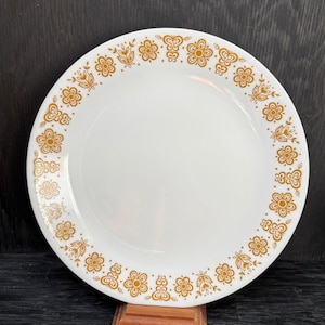 Peut inclure: Une assiette plate en céramique blanche avec un motif floral doré autour du bord.