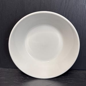 Op de afbeelding: Een witte keramische kom met een gladde, afgeronde rand. De kom is leeg en heeft een glanzende afwerking.