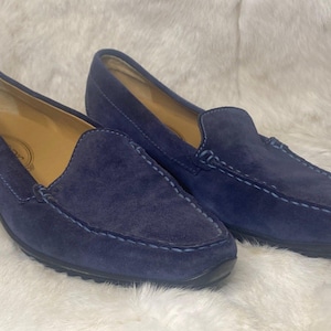 Puede incluir: Un par de mocasines de ante azul marino. Los zapatos tienen un dise&ntilde;o cl&aacute;sico sin cordones con punta redonda y tac&oacute;n bajo. Las costuras blancas acent&uacute;an las costuras. El interior es de color beige claro.