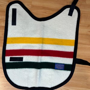 May include: A white saddle pad with a black border and straps. It has horizontal stripes in yellow, red, and green. A blue label with the word "PENDLETON" is visible on the pad.