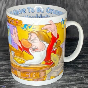 May include: White ceramic coffee mug featuring a colourful illustration of Grumpy from Snow White and the Seven Dwarfs. The mug has a handle and the text "I Have To Be Grumpy, Wouldn't You?" printed on the front.