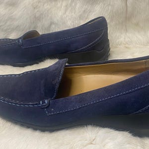 Puede incluir: Un par de mocasines de ante azul marino. Los zapatos tienen un dise&ntilde;o cl&aacute;sico sin cordones con punta redondeada y detalles cosidos en la parte superior. Las suelas son negras y el interior es de color beige claro.