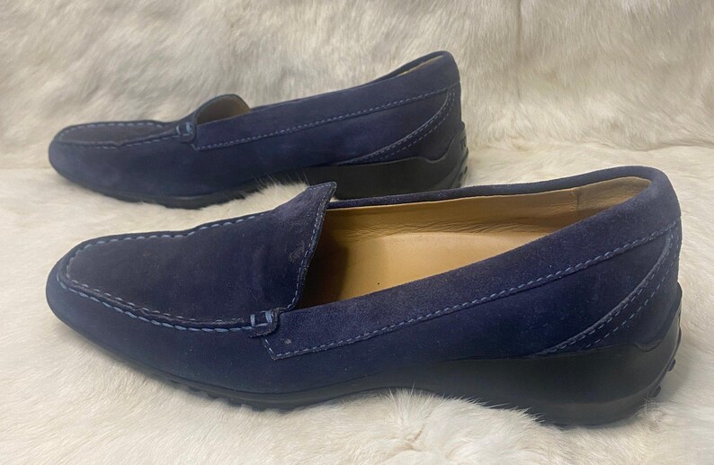 Puede incluir: Un par de mocasines de ante azul marino. Los zapatos tienen un dise&ntilde;o cl&aacute;sico sin cordones con punta redondeada y detalles cosidos en la parte superior. Las suelas son negras y el interior es de color beige claro.