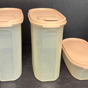 Op de afbeelding: Drie beige plastic voedselopslagcontainers met bijpassende deksels. Twee zijn hoog en rechthoekig, en één is korter en ovaal van vorm. De deksels hebben een iets donkerdere tint dan de containers.