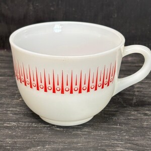 May include: White ceramic mug with a red geometric pattern around the rim. The pattern features a series of red triangles with circles at the base.
