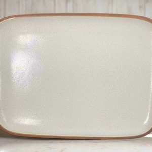 Puede incluir: Plato rectangular de cerámica blanquecina con textura moteada y borde marrón. Las esquinas son redondeadas. El plato es adecuado para servir alimentos.
