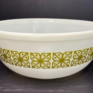 Puede incluir: Bol para mezclar blanco con un patrón floral verde oliva. El bol tiene forma redondeada y superficie lisa. El diseño floral se repite alrededor del exterior del bol, agregando un elemento decorativo a los utensilios de cocina. El diámetro es de unos 20 cm.