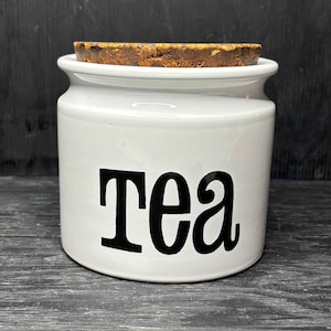 Puede incluir: Tarro de té de cerámica blanca con tapa de corcho y la palabra "Tea" en letras negras.