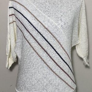 Puede incluir: Un suéter de punto blanco con un patrón diagonal de rayas negras y marrones. El suéter tiene un corte holgado y una longitud ligeramente recortada.