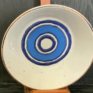 Könnte beinhalten: Eine weiße Keramikschüssel mit einem konzentrischen Kreisdesign in Blau und Weiß. Die Schüssel hat eine gesprenkelte Glasur und einen braunen Rand.