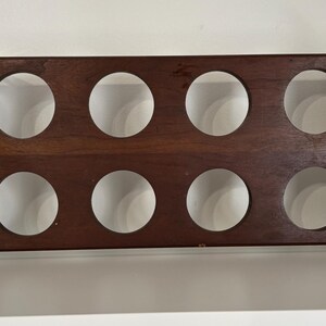 May include: A wooden wine rack with eight circular openings. The rack is made of dark brown wood and has silver metal handles on each end. The handles are curved and attached with rivets. The rack is designed to hold wine bottles.