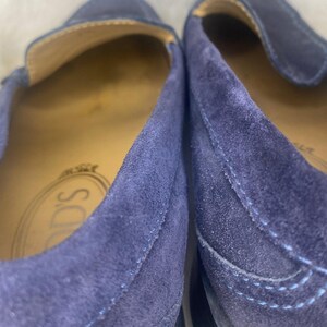 Puede incluir: Primer plano de dos mocasines de ante azul marino. El interior de los zapatos es de color beige claro. La marca "TOD'S" es visible en la plantilla. Los zapatos tienen un dise&ntilde;o cl&aacute;sico sin cordones.