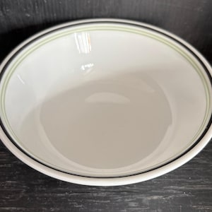 Puede incluir: Un tazón de cerámica blanco con un borde negro y verde. El tazón está vacío y listo para ser usado.