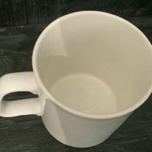 May include: A white ceramic mug with a rounded handle. The mug is empty and ready to be filled with a hot beverage.