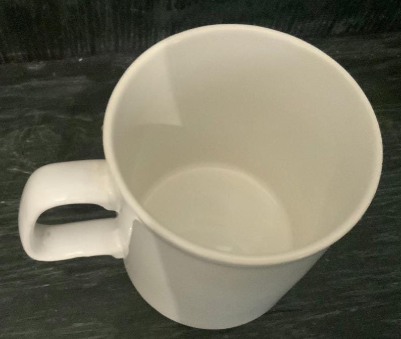 May include: A white ceramic mug with a rounded handle. The mug is empty and ready to be filled with a hot beverage.
