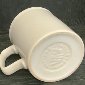 May include: White ceramic mug with a handle. The bottom of the mug has a circular mark with the text "MADE IN ENGLAND" in a circle.