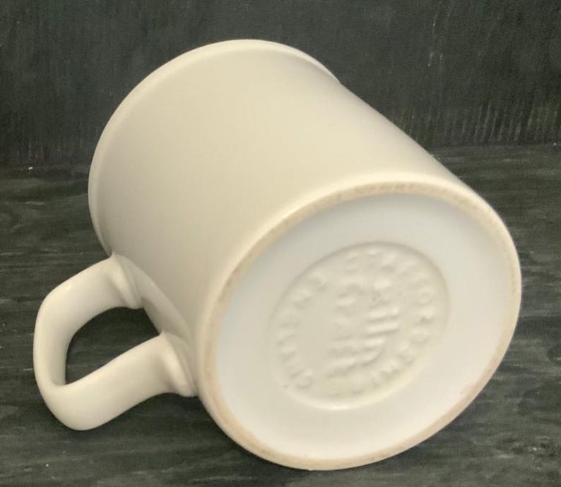 May include: White ceramic mug with a handle. The bottom of the mug has a circular mark with the text "MADE IN ENGLAND" in a circle.