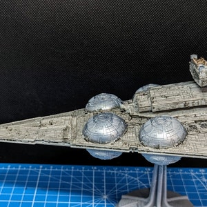 May include: A detailed model of a Star Destroyer spaceship, painted in a silver and gray color scheme. The model is mounted on a stand and features intricate details, including engine nacelles and a bridge.