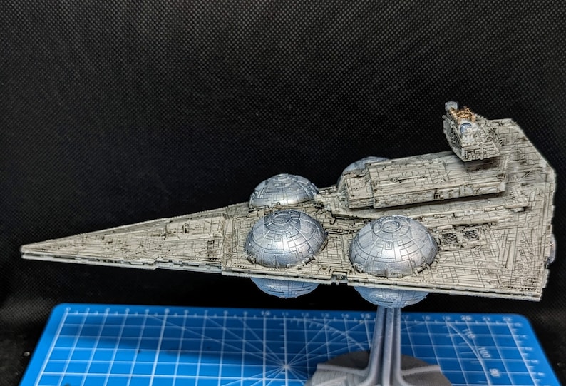 May include: A detailed model of a Star Destroyer spaceship, painted in a silver and gray color scheme. The model is mounted on a stand and features intricate details, including engine nacelles and a bridge.