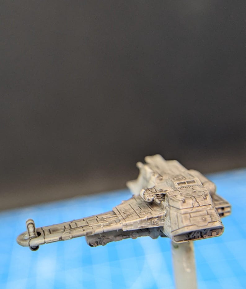 Op de afbeelding: Een wit geverfd miniatuurmodel van een ruimteschip met een gedetailleerd ontwerp. Het model staat op een transparante plastic standaard.