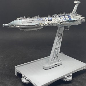 Puede incluir: Un modelo gris y azul de una nave espacial de Star Wars en un soporte gris. La nave espacial tiene un cuerpo largo y delgado con una nariz puntiaguda y un ala grande y plana en la parte superior. El soporte es de pl&aacute;stico y tiene una base rectangular.