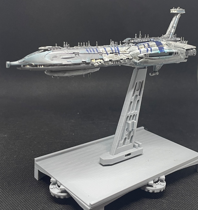 Puede incluir: Un modelo gris y azul de una nave espacial de Star Wars en un soporte gris. La nave espacial tiene un cuerpo largo y delgado con una nariz puntiaguda y un ala grande y plana en la parte superior. El soporte es de pl&aacute;stico y tiene una base rectangular.
